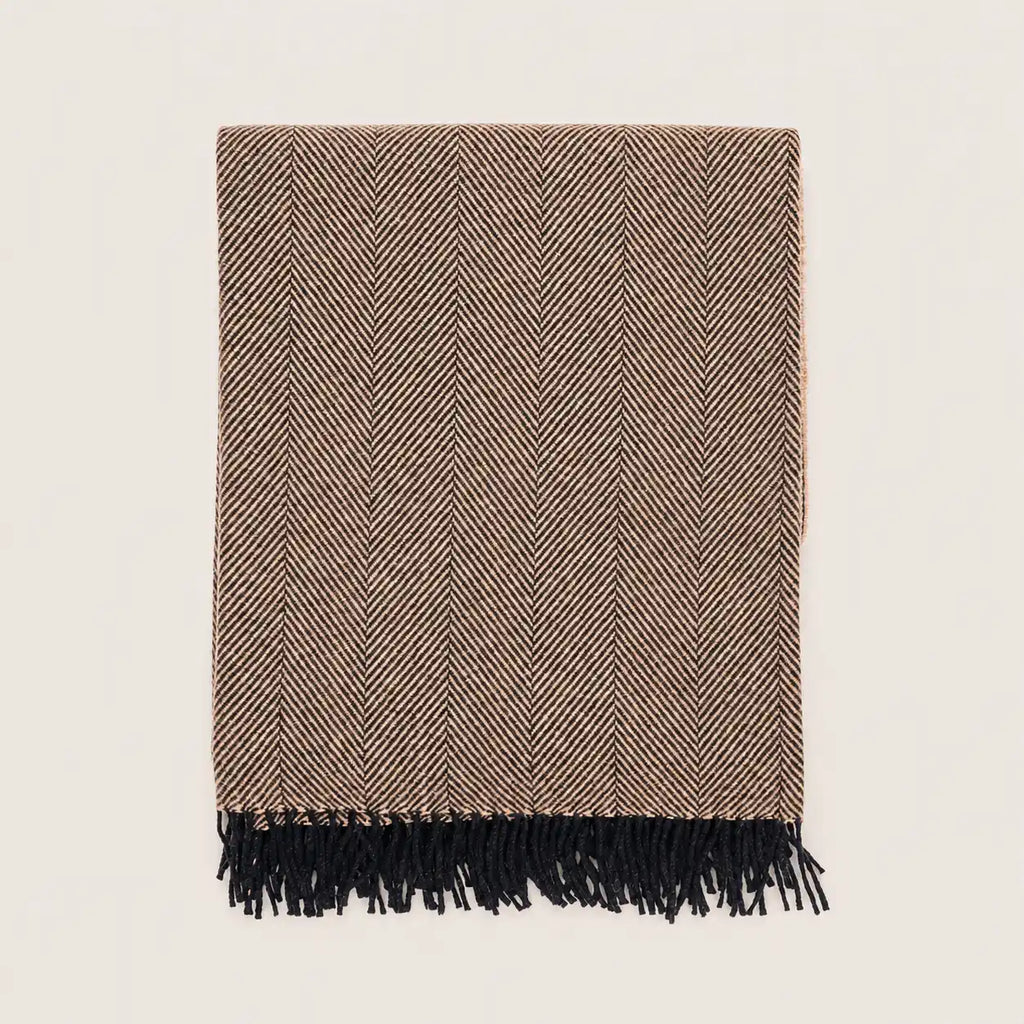 A rectangular woven throw blanket with a brown and beige herringbone pattern and black fringe along one edge, shown flat against a light off-white background.