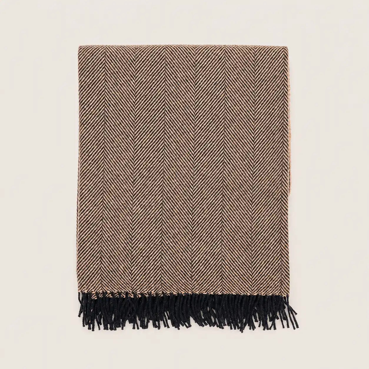 A rectangular woven throw blanket with a brown and beige herringbone pattern and black fringe along one edge, shown flat against a light off-white background.