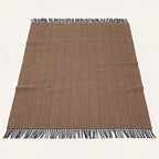 A rectangular woven blanket throw in a warm taupe-brown colour with a subtle herringbone pattern and black fringe on all four ends, laid flat against a light off-white background.