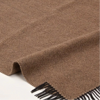A brown woven blanket throw with a herringbone pattern and black fringe, laid out on a light background.