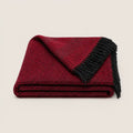 A folded red and black herringbone throw blanket with black fringe, displayed on a light beige background.