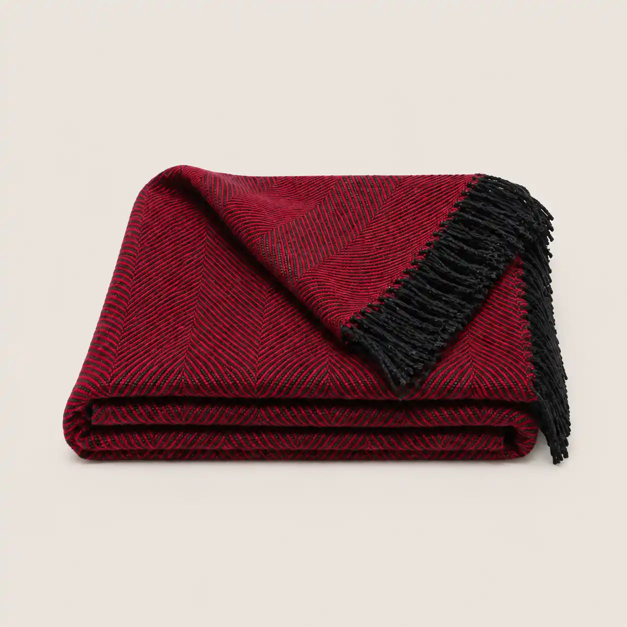 A folded red and black herringbone throw blanket with black fringe, displayed on a light beige background.