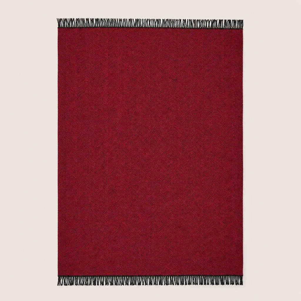 A rectangular deep red woven throw blanket with black and white fringe tassels on the top and bottom edges, shown flat against a light beige background.