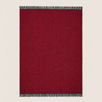A rectangular deep red woven throw blanket with black and white fringe tassels on the top and bottom edges, shown flat against a light beige background.