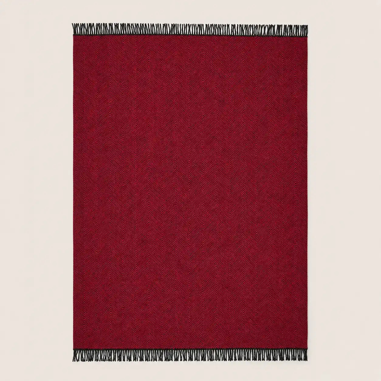 A rectangular deep red woven throw blanket with black and white fringe tassels on the top and bottom edges, shown flat against a light beige background.