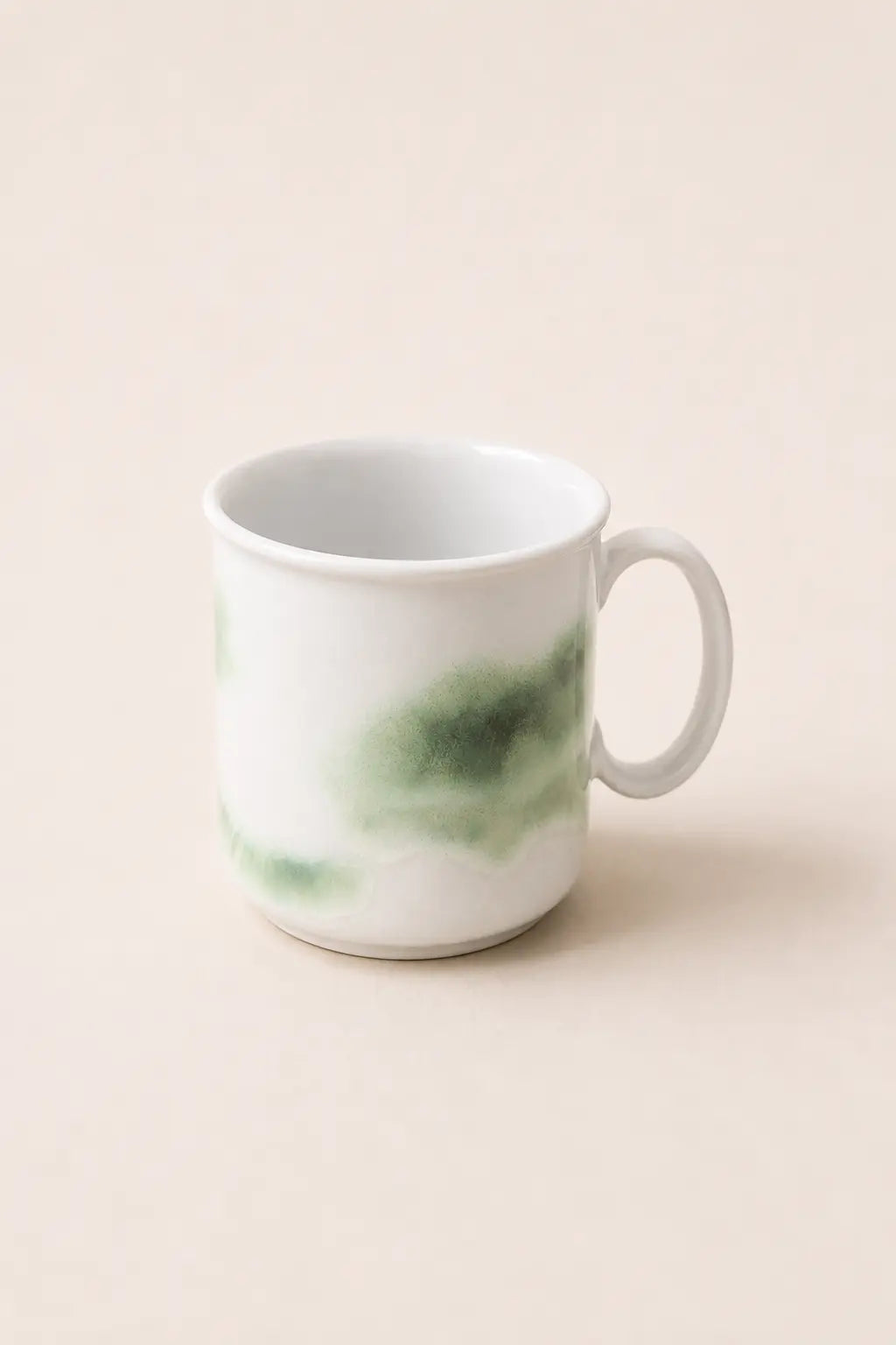 A white ceramic mug with a green watercolor-style wash on the side, set against a solid light beige background.
