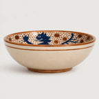 A ceramic bowl with a cream-colored exterior and an interior decorated with blue dragon motifs and brown polka dots, set against a plain light gray background.