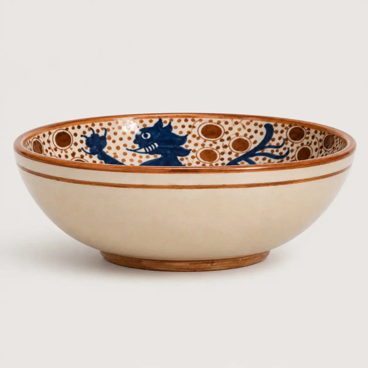 A ceramic bowl with a cream-colored exterior and an interior decorated with blue dragon motifs and brown polka dots, set against a plain light gray background.