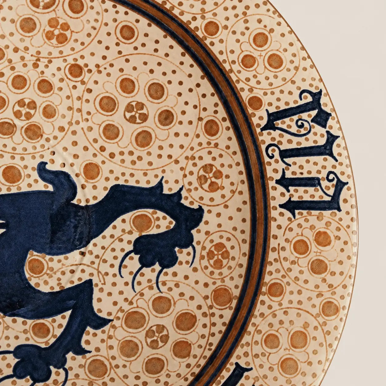 A round ceramic plate with a speckled beige and brown glaze, featuring a central dark blue dragon motif and Roman numerals around the rim, set against a plain light beige background.