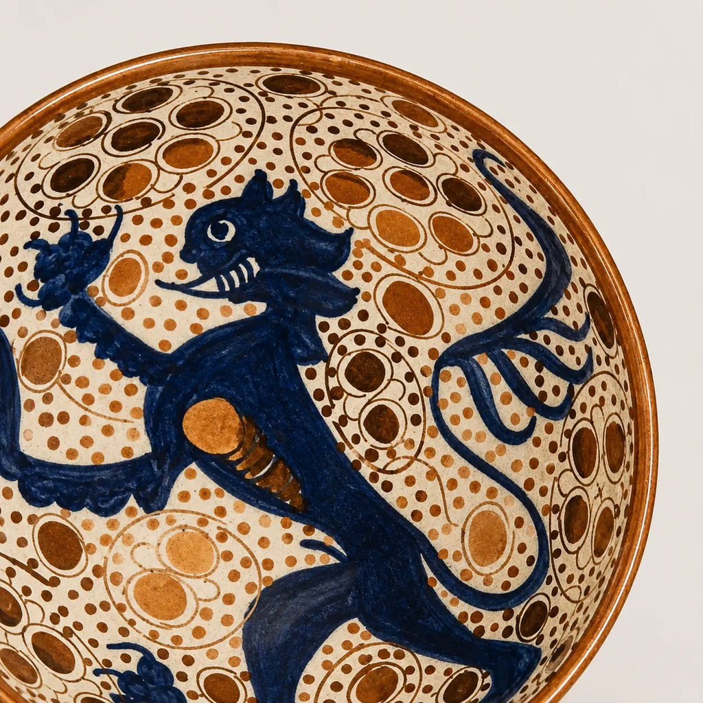 Close-up of a ceramic bowl featuring a dark blue rampant lion motif over a cream background decorated with brown dotted circles and a brown rim.
