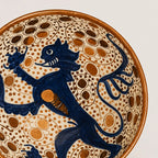 Close-up of a ceramic bowl featuring a dark blue rampant lion motif over a cream background decorated with brown dotted circles and a brown rim.