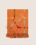 An orange plaid throw blanket with fringe, folded diagonally on a light beige background.