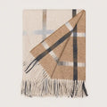 A folded woven wool throw blanket with fringe, featuring a classic check pattern in beige, brown, white, and dark gray on a light cream background.