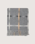 A gray woven throw blanket with a classic plaid pattern in white, black, and tan, finished with fringed edges, shown flat against a light beige background.