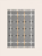 A rectangular merino wool gray woven throw blanket with a plaid pattern, featuring vertical metallic gold stripes, horizontal white stripes, and fringed edges on all sides, shown flat against a light beige background.