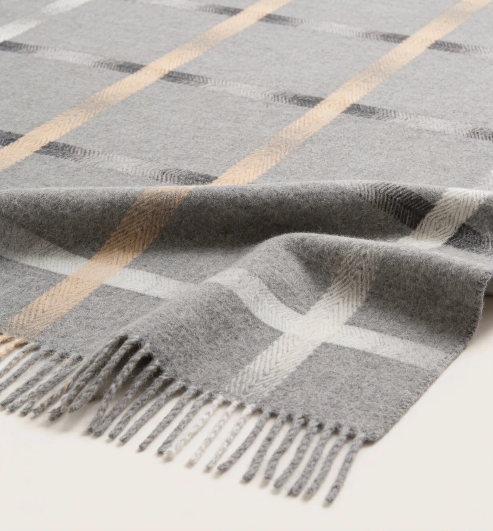 A gray plaid wool throw blanket with fringed edges, featuring diagonal stripes in beige, white, and dark gray on a light cream background.