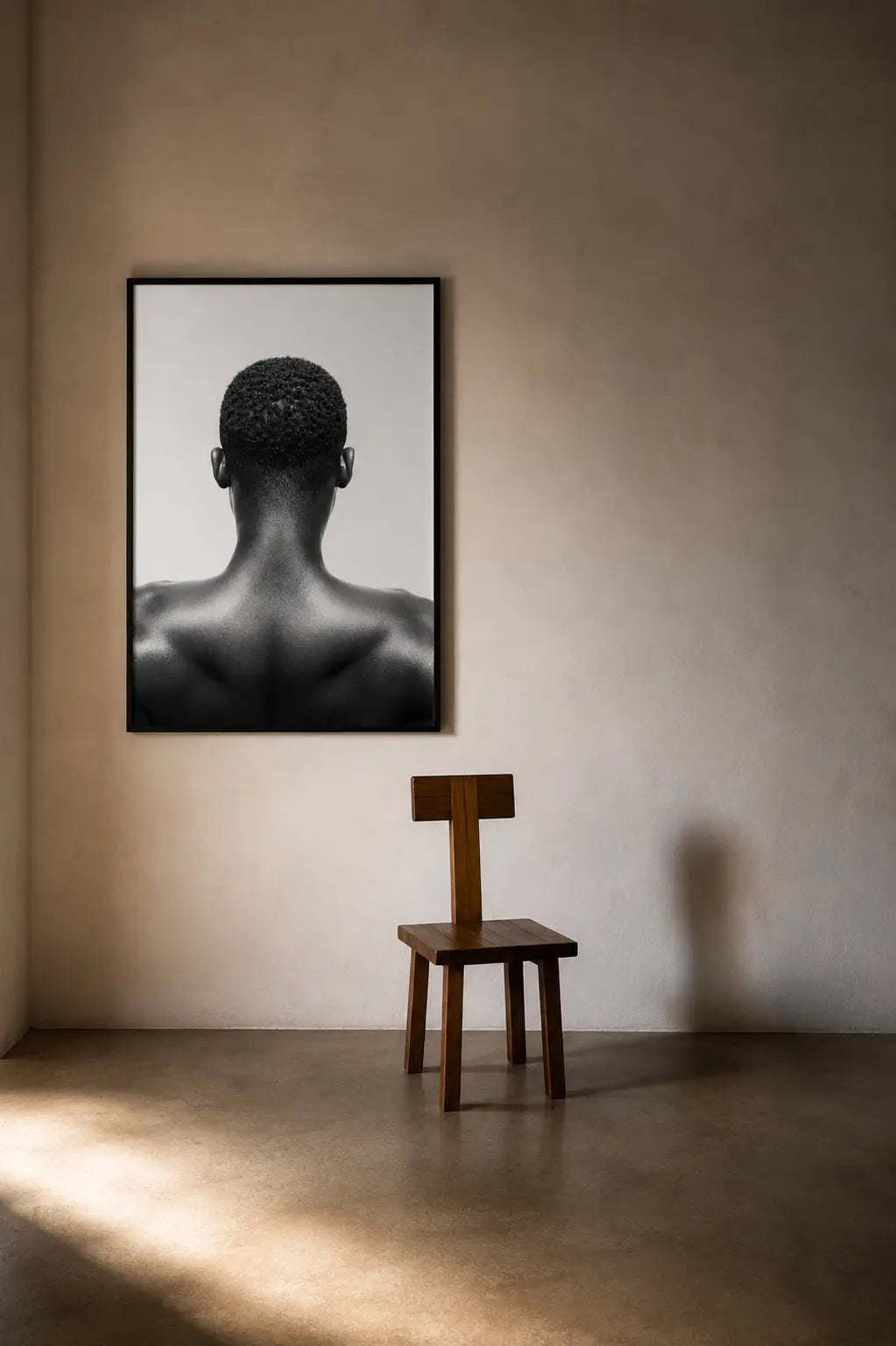 Black and white studio photograph of a man's bare back and neck, viewed from behind, with short curly hair and no visible clothing against a plain light background.