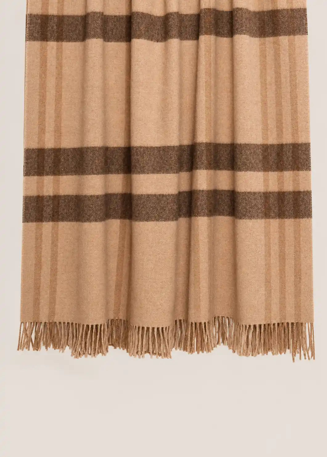 A close-up of a throw blanket with a beige and brown check pattern and fringed edges, shown against a light gray background.
