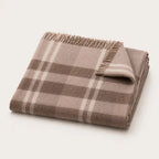 A folded plaid throw blanket with fringed edges, shown on a clean off-white background. The pattern features shades of taupe, brown, and cream.