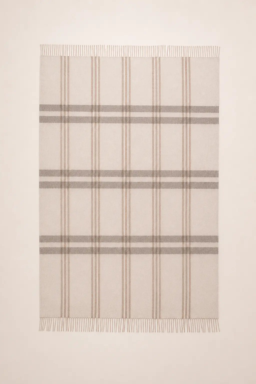 A rectangular woven throw blanket with fringed edges, featuring a classic plaid pattern in beige, taupe, and light brown on a cream background.