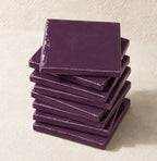 A stack of square plum ceramic tiles on a textured beige surface.