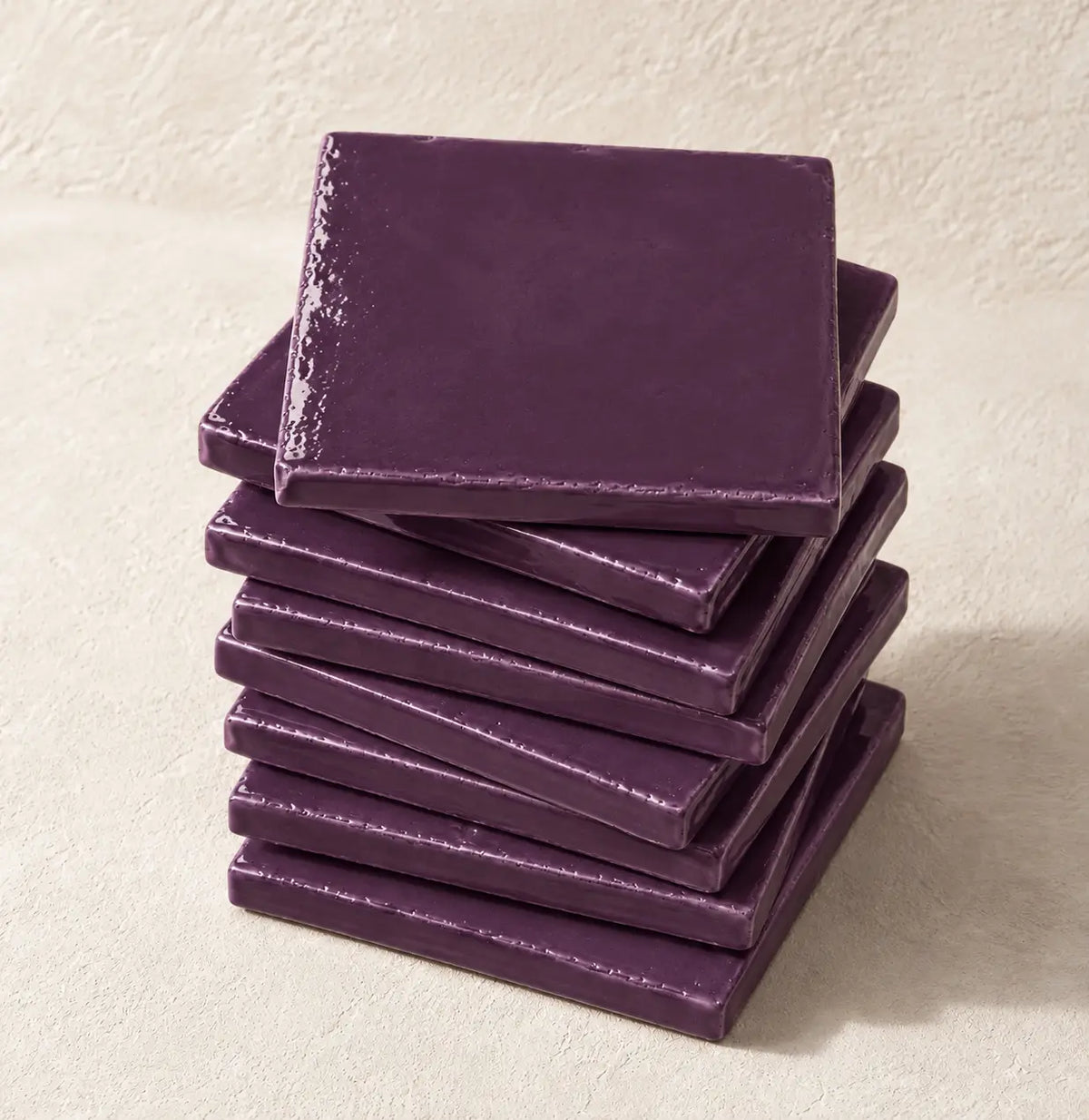 A stack of square plum ceramic tiles on a textured beige surface.