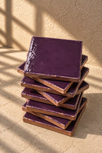 A stack of square plum ceramic tiles on a textured beige surface.