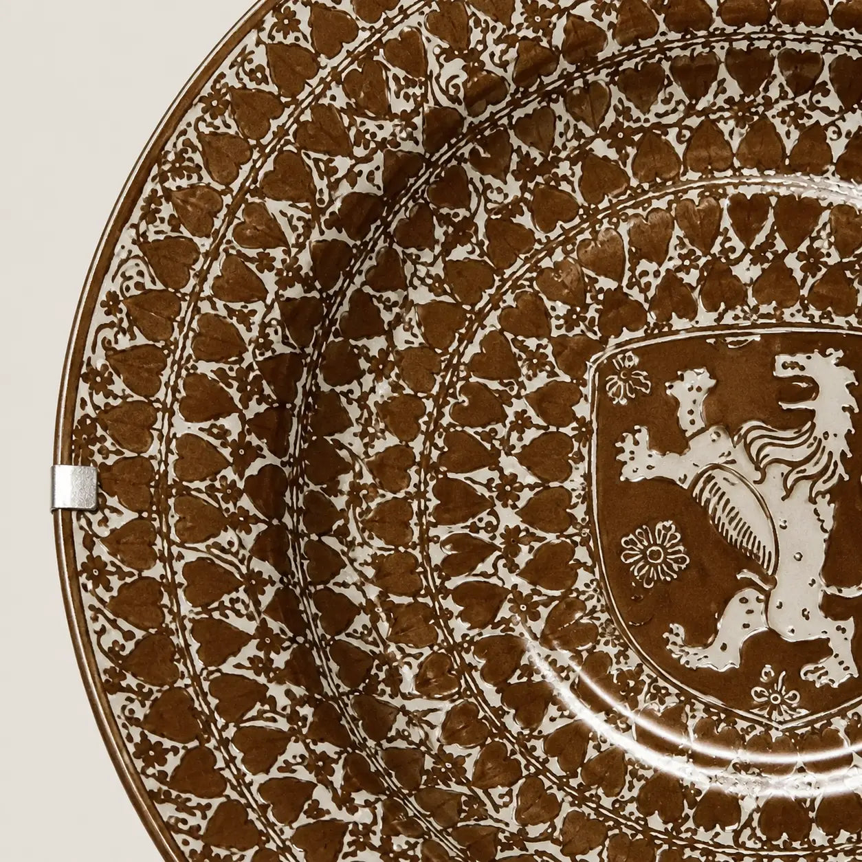 A close-up of a decorative ceramic plate featuring a brown and white hand-painted pattern with a heraldic lion crest in the center.