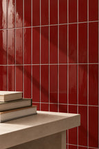 Glossy red tiles arranged in a grid pattern on a wall, with a light beige stone ledge in the foreground holding a stack of books.