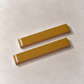 Two glossy amber yellow rectangular ceramic tiles with a textured beige base, arranged diagonally on a light beige textured surface.