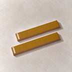 Two glossy amber yellow rectangular ceramic tiles with a textured beige base, arranged diagonally on a light beige textured surface.