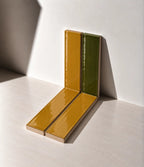 Glossy Amber Yellow and Moss Green handmade ceramic tiles arranged against a white wall in natural sunlight.