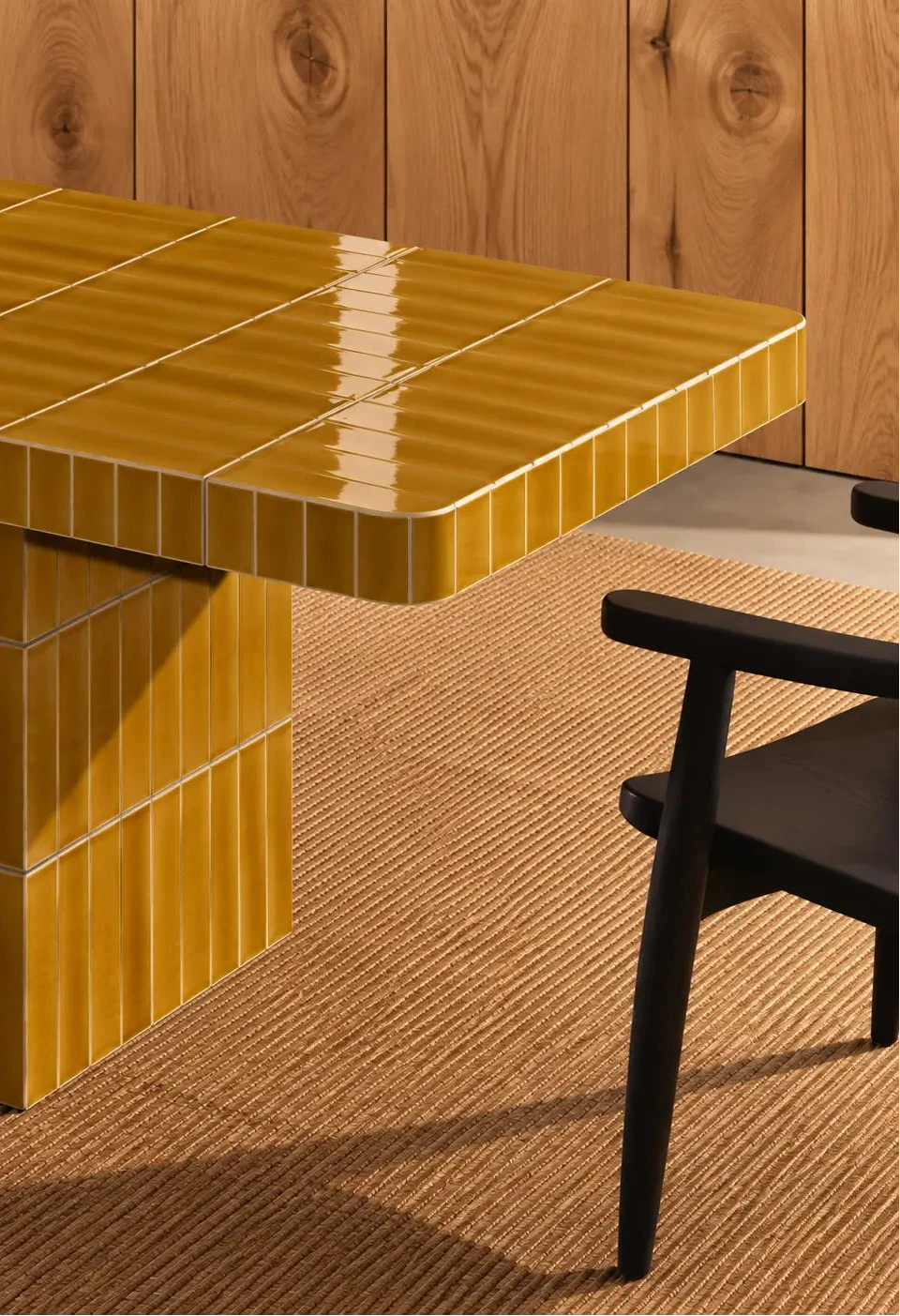 Glossy amber yellow rectangular ceramic tiles covering a dining table, paired with a dark wood chair and natural woven rug.
