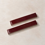 Two glossy rectangular cabinet pulls in a deep burgundy red finish, displayed diagonally on a textured beige surface.