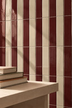 Glossy dark red rectangular wall tiles arranged in a grid pattern, with a light stone ledge in the foreground holding a stack of books.
