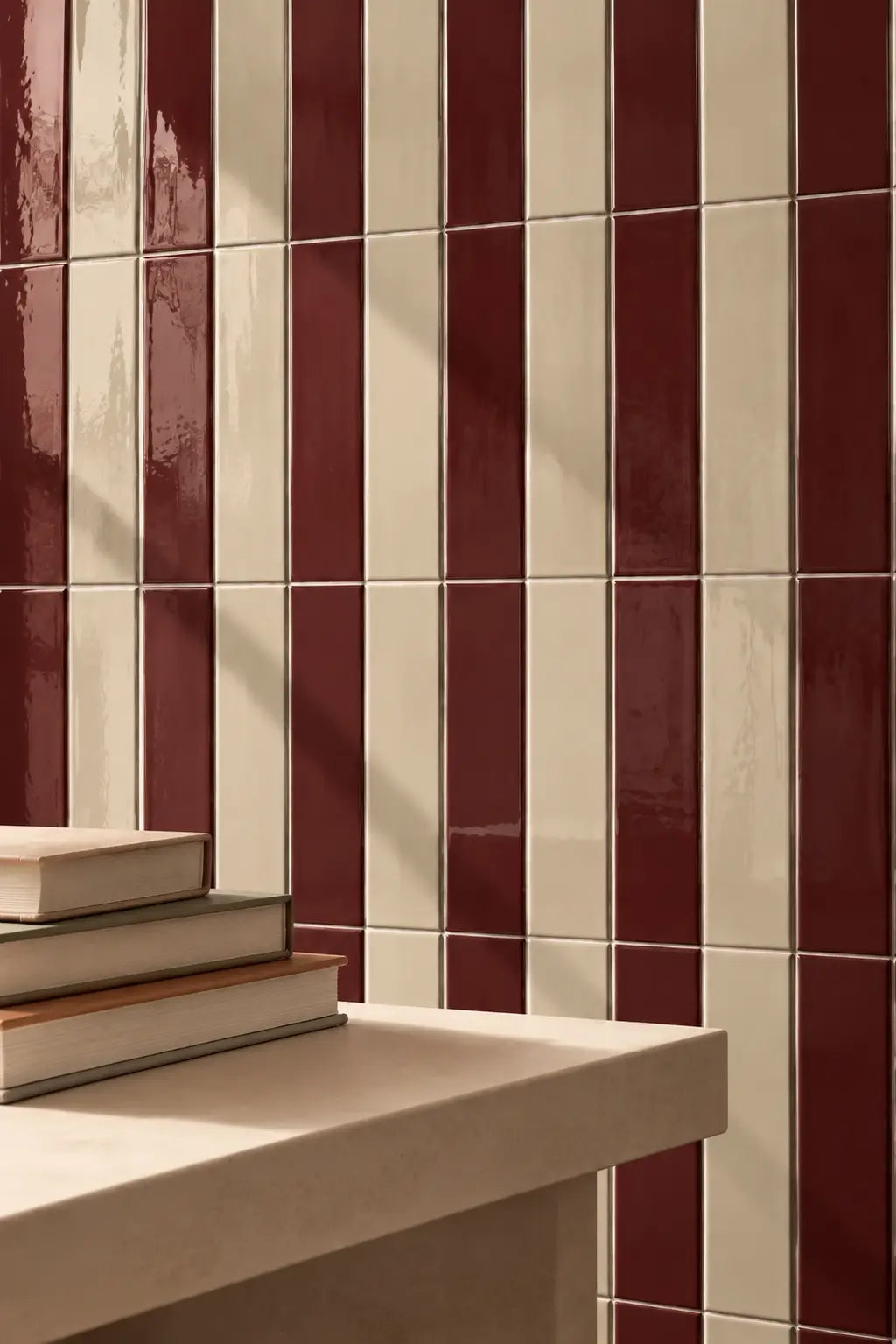 Glossy dark red rectangular wall tiles arranged in a grid pattern, with a light stone ledge in the foreground holding a stack of books.
