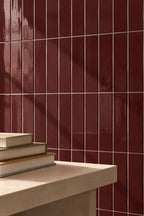 Glossy dark red rectangular wall tiles arranged in a grid pattern, with a light stone ledge in the foreground holding a stack of books.