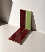Glossy Burgundy Red and Sage Green handmade ceramic tiles arranged against a white wall in natural sunlight.