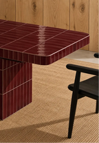
Glossy burgundy red rectangular ceramic tiles covering a dining table, paired with a dark wood chair and natural woven rug.