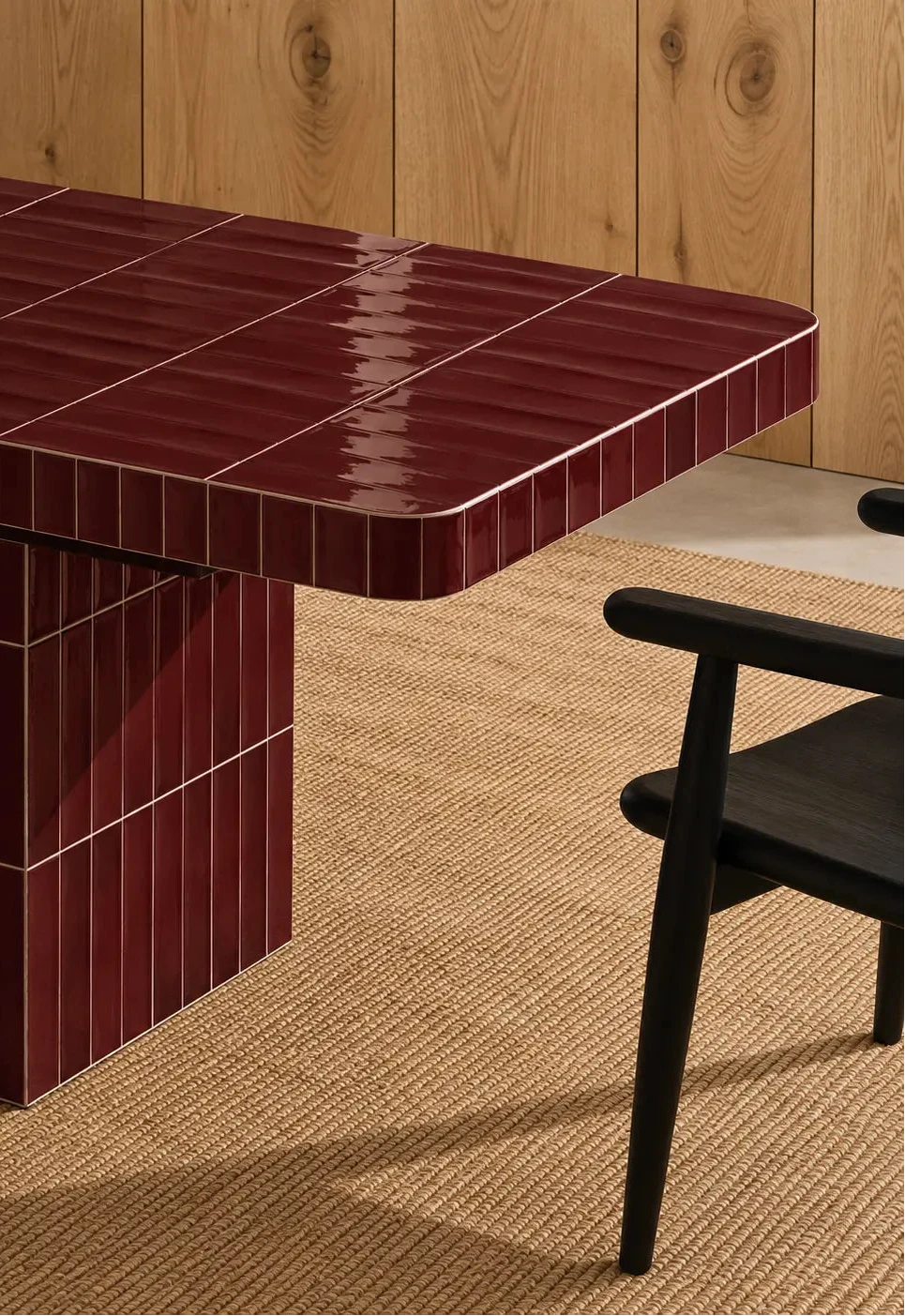 
Glossy burgundy red rectangular ceramic tiles covering a dining table, paired with a dark wood chair and natural woven rug.