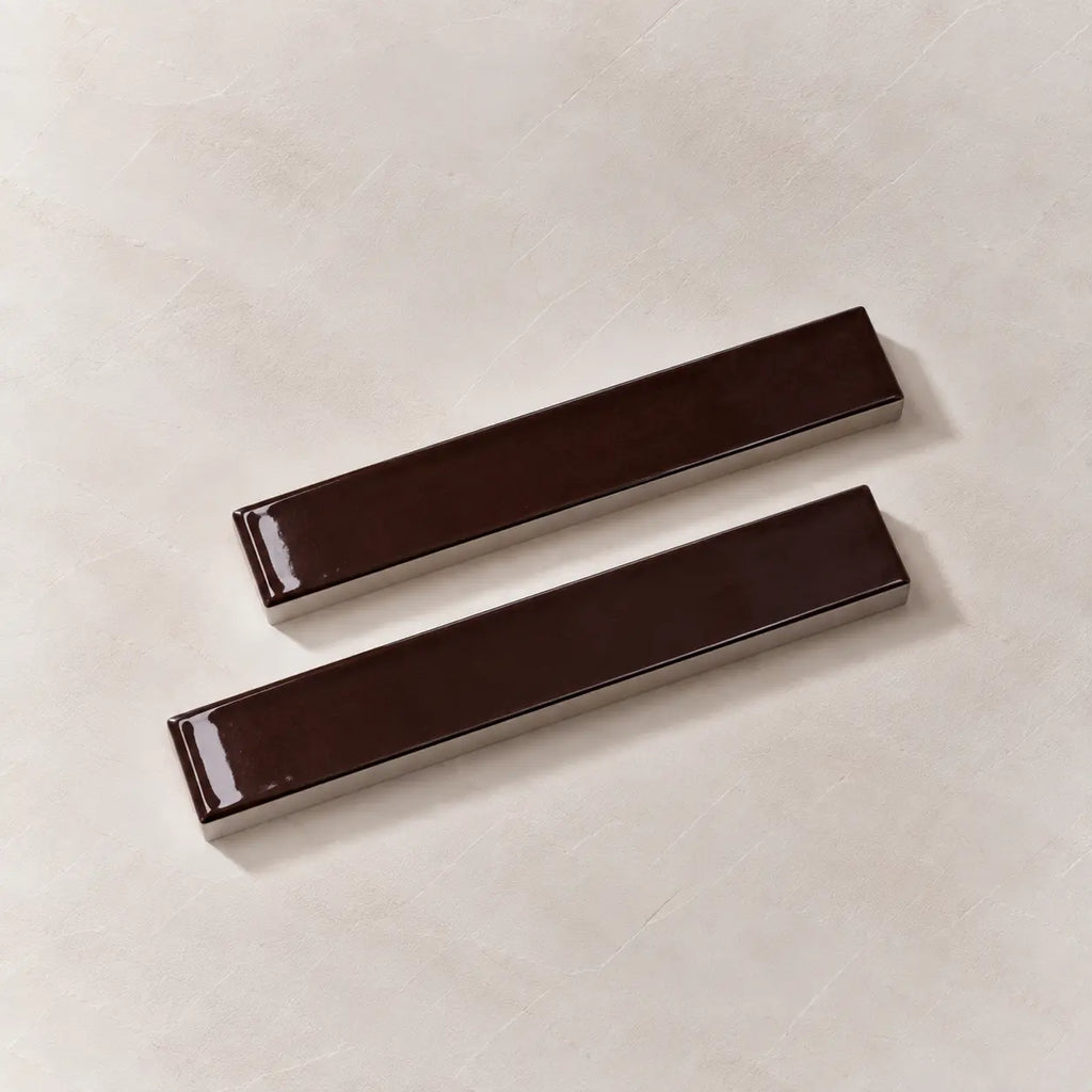 Two glossy dark brown rectangular ceramic tiles with rounded ends, displayed diagonally on a light beige textured background.