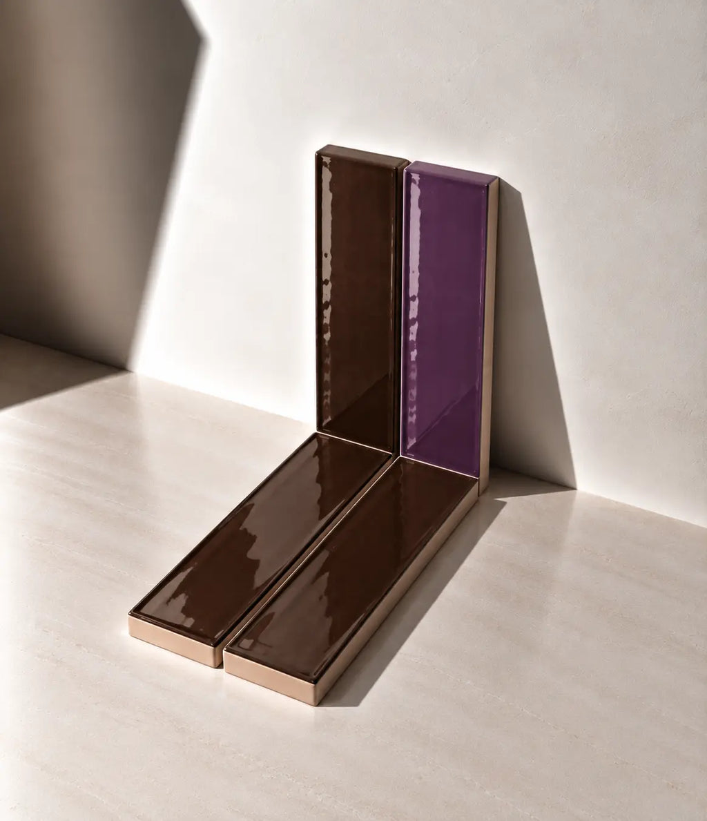 Glossy Chocolate brown and Plum handmade ceramic tiles arranged against a white wall in natural sunlight.