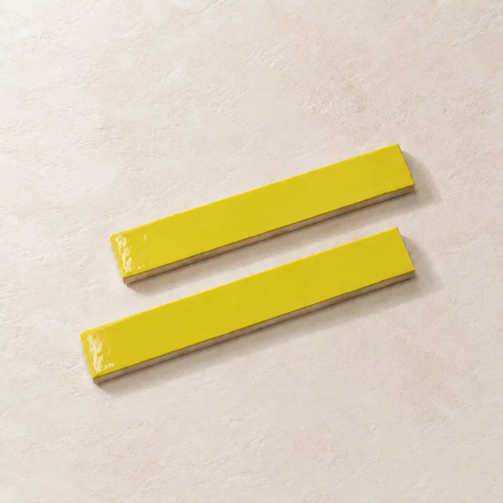 Two glossy citron yellow rectangular ceramic tiles with a textured beige base, arranged diagonally on a light beige textured surface.
