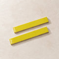 Two glossy citron yellow rectangular ceramic tiles with a textured beige base, arranged diagonally on a light beige textured surface.