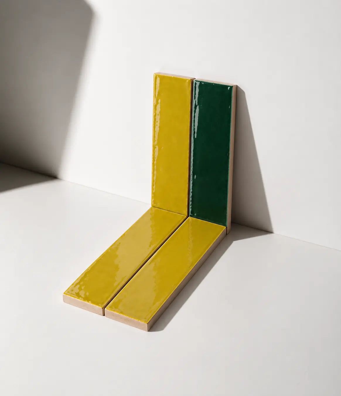 Glossy Citron Yellow and Forest Green handmade ceramic tiles arranged against a white wall in natural sunlight.