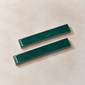 Two glossy dark green rectangular ceramic tiles with silver metal backings, displayed diagonally on a textured beige background.