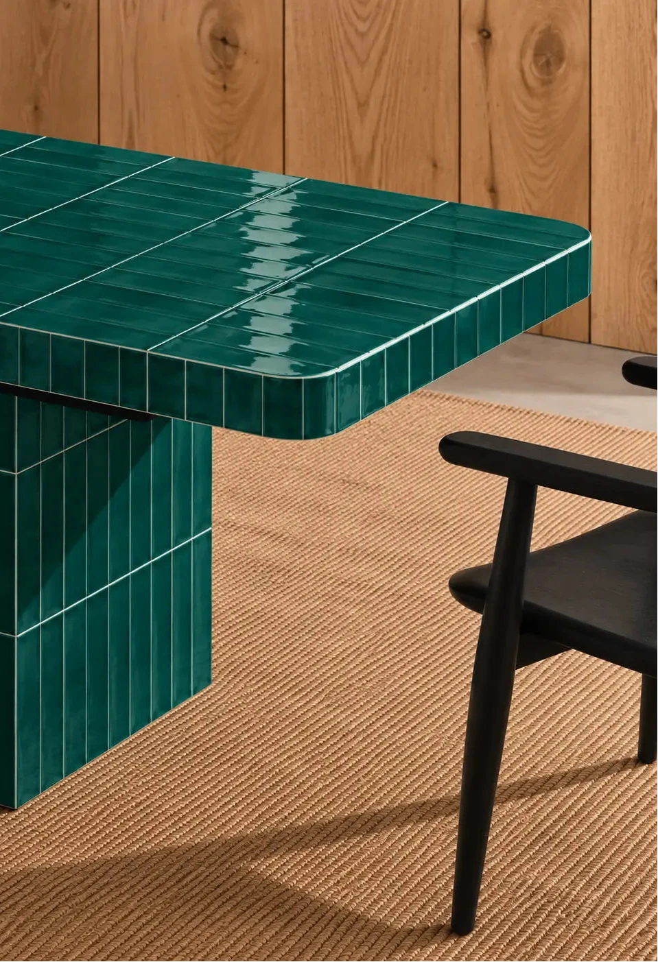 
Glossy emerald green rectangular ceramic tiles covering a dining table, paired with a dark wood chair and natural woven rug.