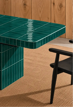 
Glossy emerald green rectangular ceramic tiles covering a dining table, paired with a dark wood chair and natural woven rug.