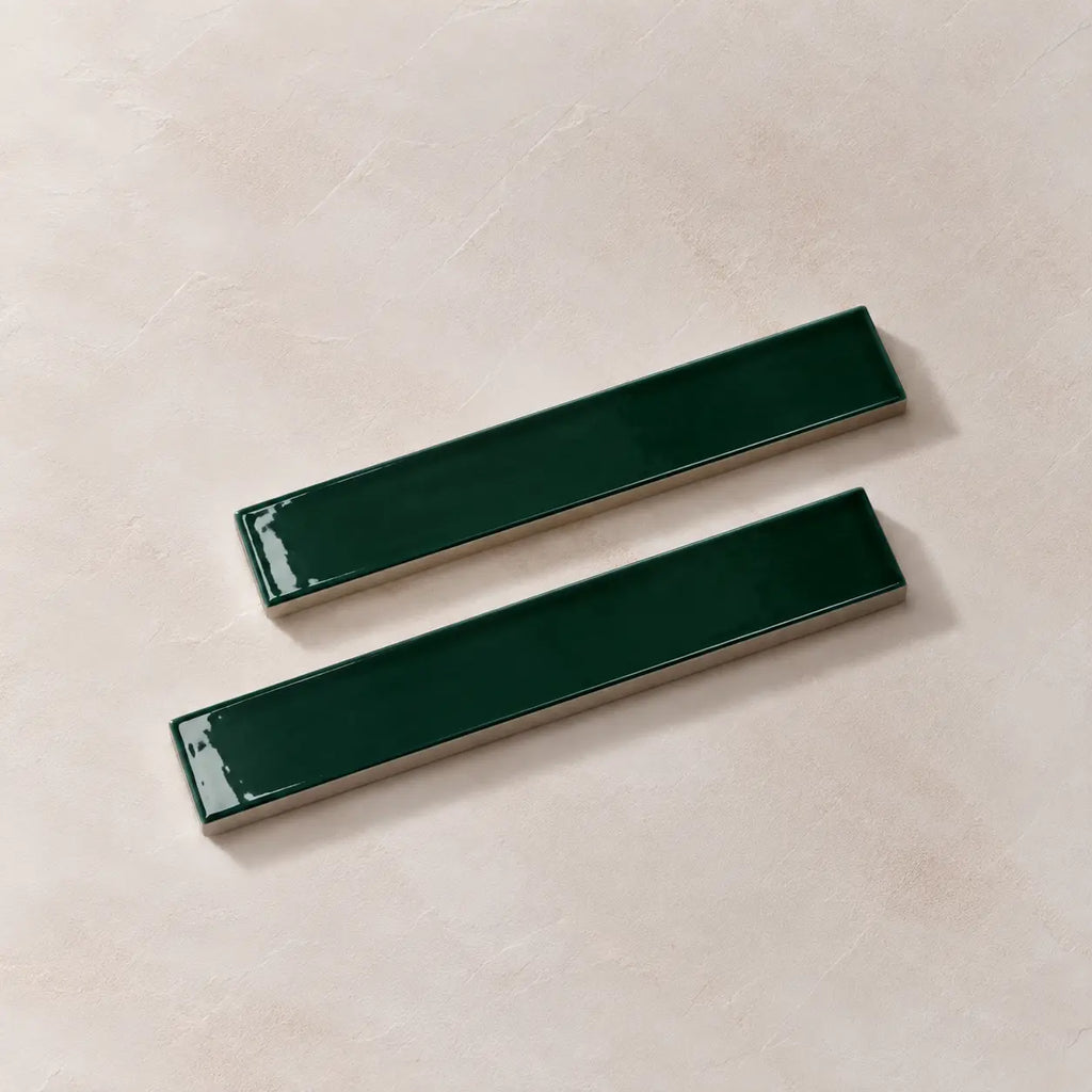 Two glossy dark green rectangular ceramic tiles with silver metallic edges, arranged diagonally on a textured beige background.