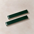 Two glossy dark green rectangular ceramic tiles with silver metallic edges, arranged diagonally on a textured beige background.